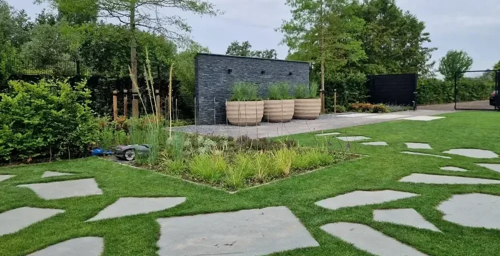 Designtuin met stapstenen door de tuin en een wand met potten ervoor.