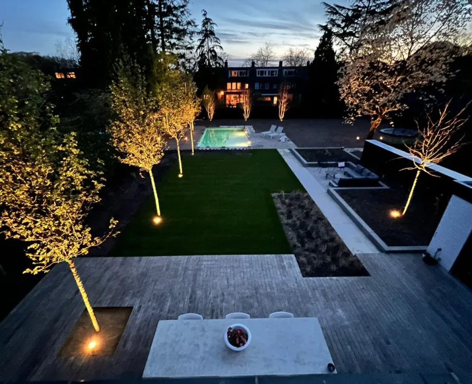 Moderne tuin met zwembad in de avond met de tuinverlichting aan. Tuinaanleg door Uw Tuin Hoveniers uit Malden.