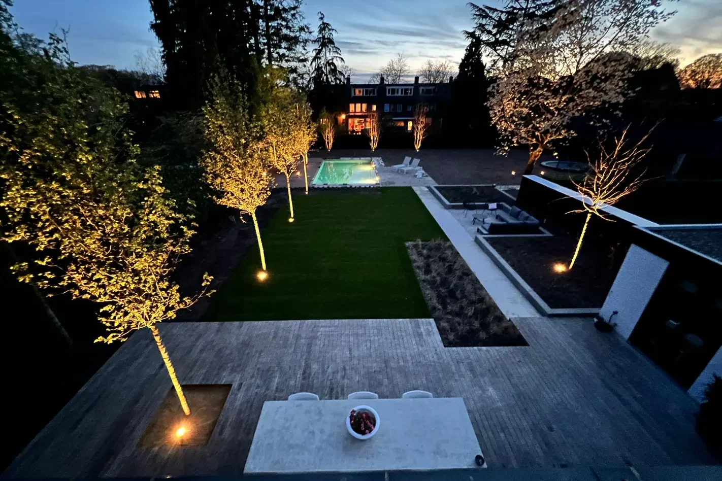 Moderne tuin met zwembad in de avond met de tuinverlichting aan. Tuinaanleg door Uw Tuin Hoveniers uit Malden.