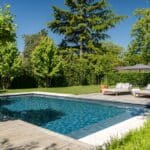 Moderne tuin met zwembad in Nijmegen. Strakke moderne tuin met groot gazon. Vlonderterras met ligbedjes, parasol. Grote bomen voor natuurlijke schaduw. Strak modern zwembad. Heerlijk zwemmen in de zomer. Tuinontwerp en tuinaanleg door Uw Tuin hoveniers uit Malden.