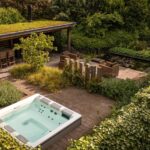 Luxe wellnesstuin in Huissen met jacuzzi, buitendouche, overkapping met haard en een vijver met luxe waterelementen. Ultiem ontspannen in deze tuin.