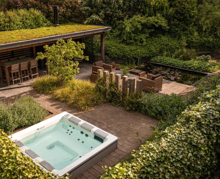 Luxe wellnesstuin in Huissen met jacuzzi, buitendouche, overkapping met haard en een vijver met luxe waterelementen. Ultiem ontspannen in deze tuin.