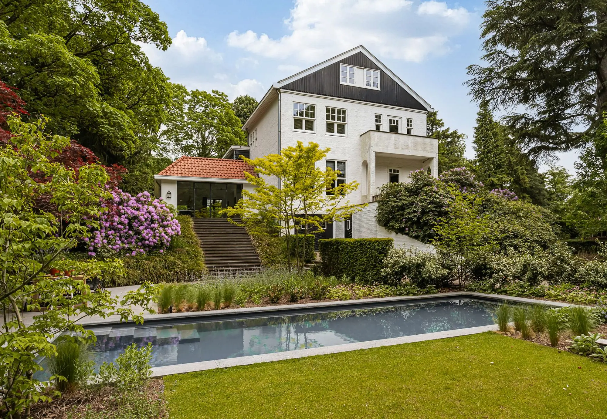 Bostuin met zwembad op de Heilige Landstichting in Nijmegen. Tuinontwerp en tuinaanleg door Uw Tuin Hoveniers uit Malden. Woonhuis als eyecather met prachtig uitzicht over de tuin. Groen is de basis. Omgeving komt de bostuin in. Veel beplanting, solitaire heesters, Rhododendrons, nieuwe beplanting in plantenborders.