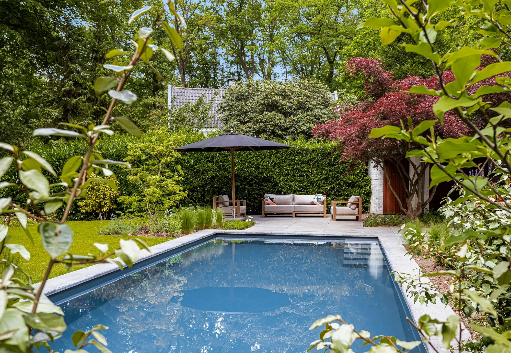 Bostuin met zwembad op de Heilige Landstichting in Nijmegen. Tuinontwerp en tuinaanleg door Uw Tuin Hoveniers uit Malden. zwembad als eyecatcher met prachtig middelpunt over de tuin. Groen is de basis. Omgeving komt de bostuin in. Veel beplanting, solitaire heesters, rode Acer, nieuwe beplanting in plantenborders.