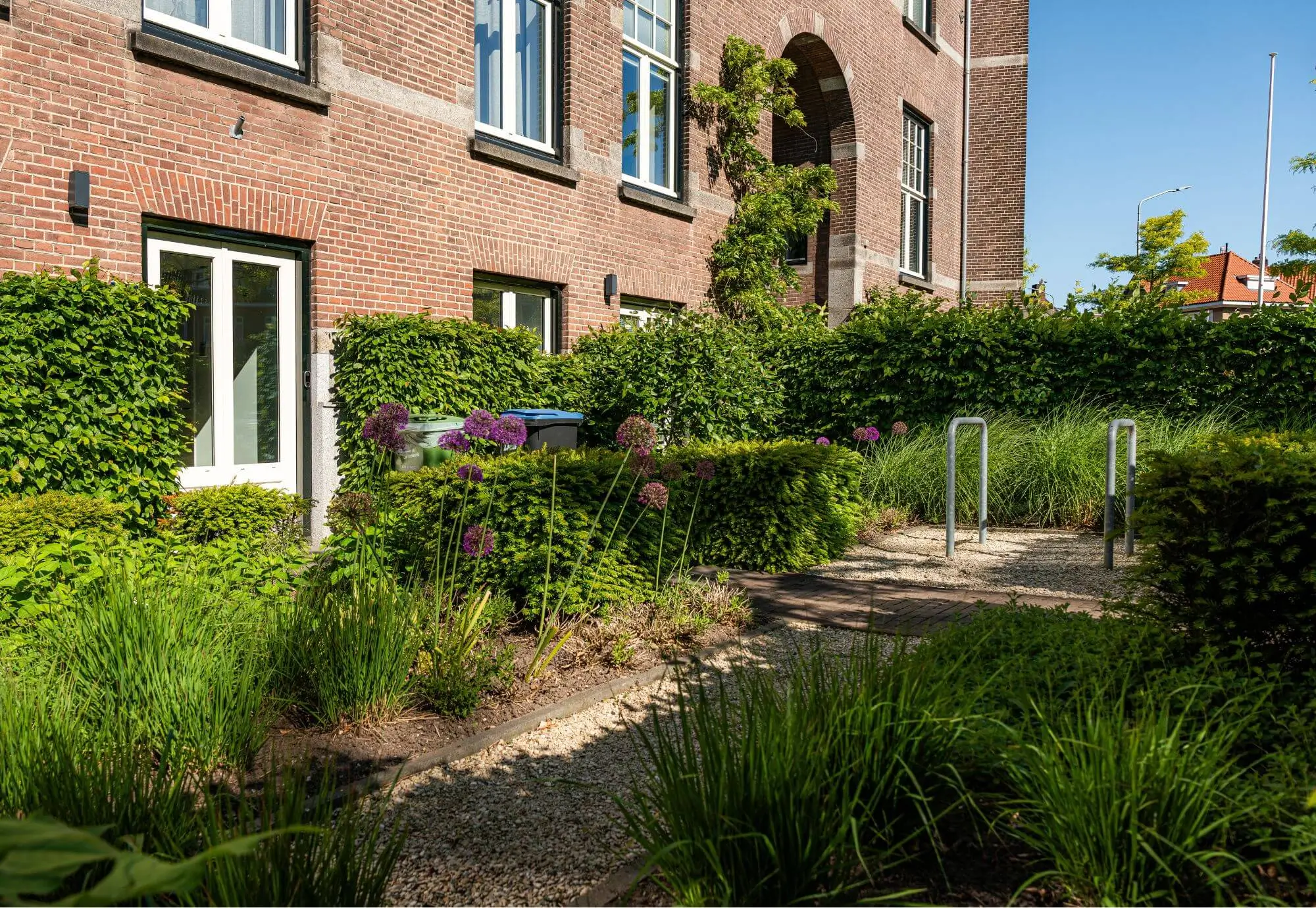 Voortuin van Cum Laude in Nijmegen. Tuinaanleg en Tuinontwerp door Uw Tuin hoveniers uit Malden. Tuinontwerp ontstaan door participatie met bewoners. Gezamelijke tuin met fietsenstalling. Veel afscherming door veel groen en kleurrijke borderbeplanting.