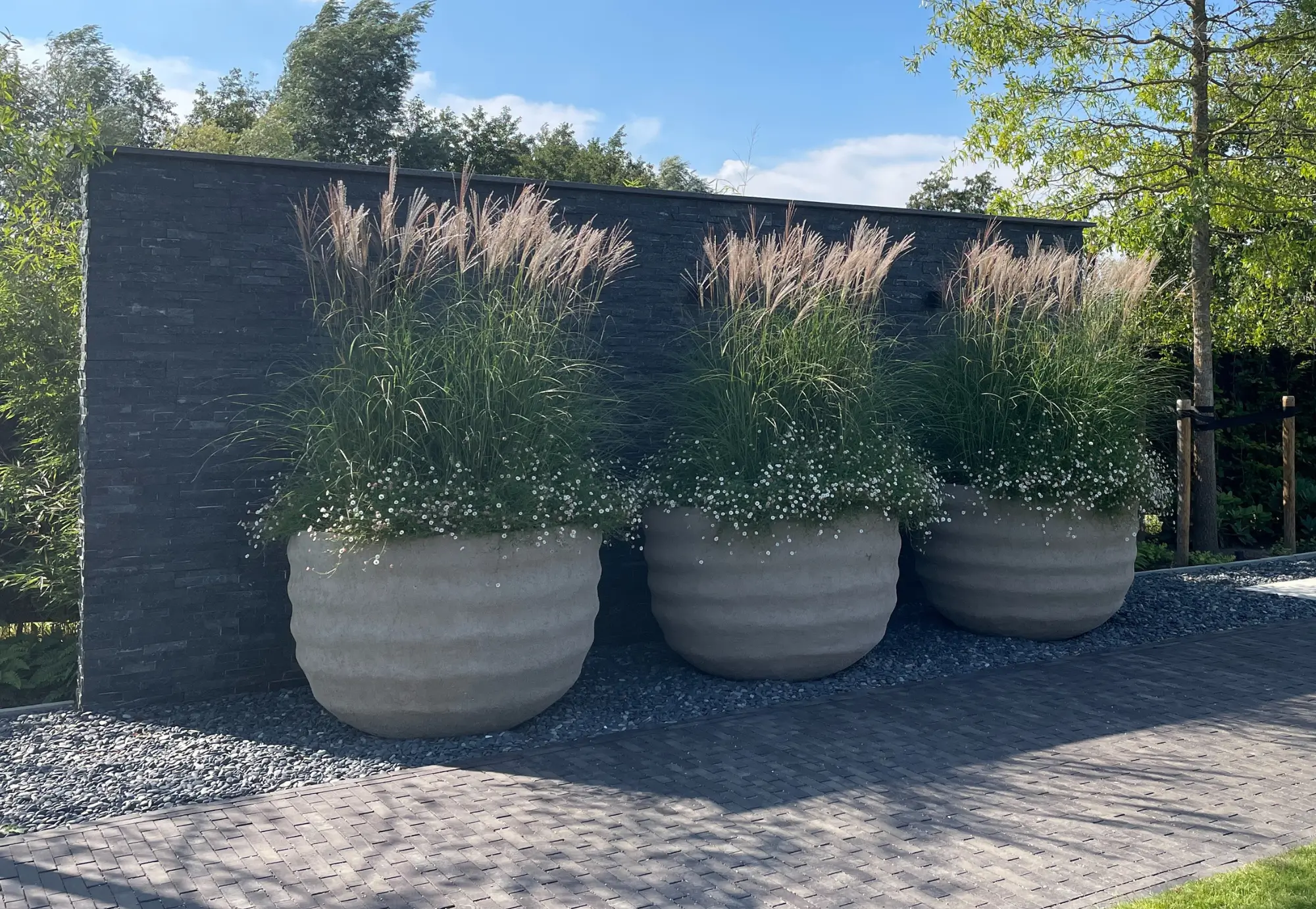 Designtuin met beplanting en een Gemetselde wand met steenstrips met grote moderne potten ervoor.