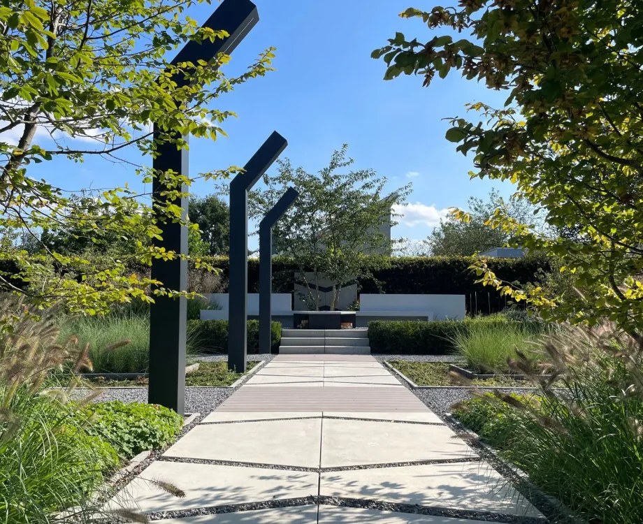 Zichtlijn door de groene Designtuin met veel weelderige beplanting met solitaire heesters, Strakke tuinelementen met Erik van Gelder Designtegels in prachtige groene beplanting. Uitgebreid verlichtingsplan met designverlichting als tuinelementen. Loungeplek met groot terras als heerlijke zithoek in de zon. Tuinontwerp en Tuinaanleg door Uw Tuin hoveniers uit Malden.