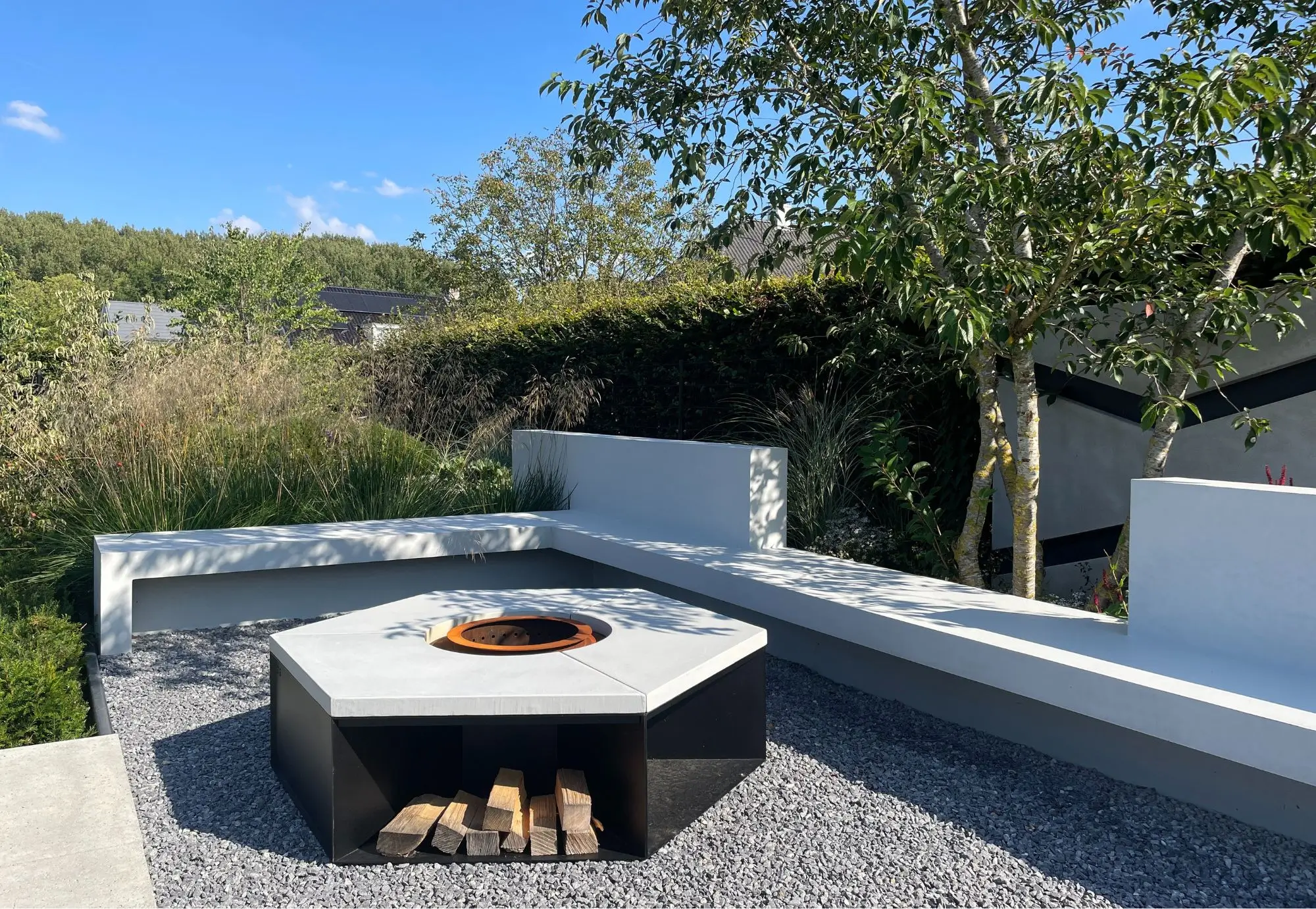 Detail van Loungeterras met een vuurelement in een designtuin. Met strakke wanden, weelderig groen, grassen, groene hagen, strakke materialen, in het groen, solitaire heesters en unieke verlichting. Tuinontwerp en Tuinaanleg door Uw Tuin Hoveniers uit Malden.