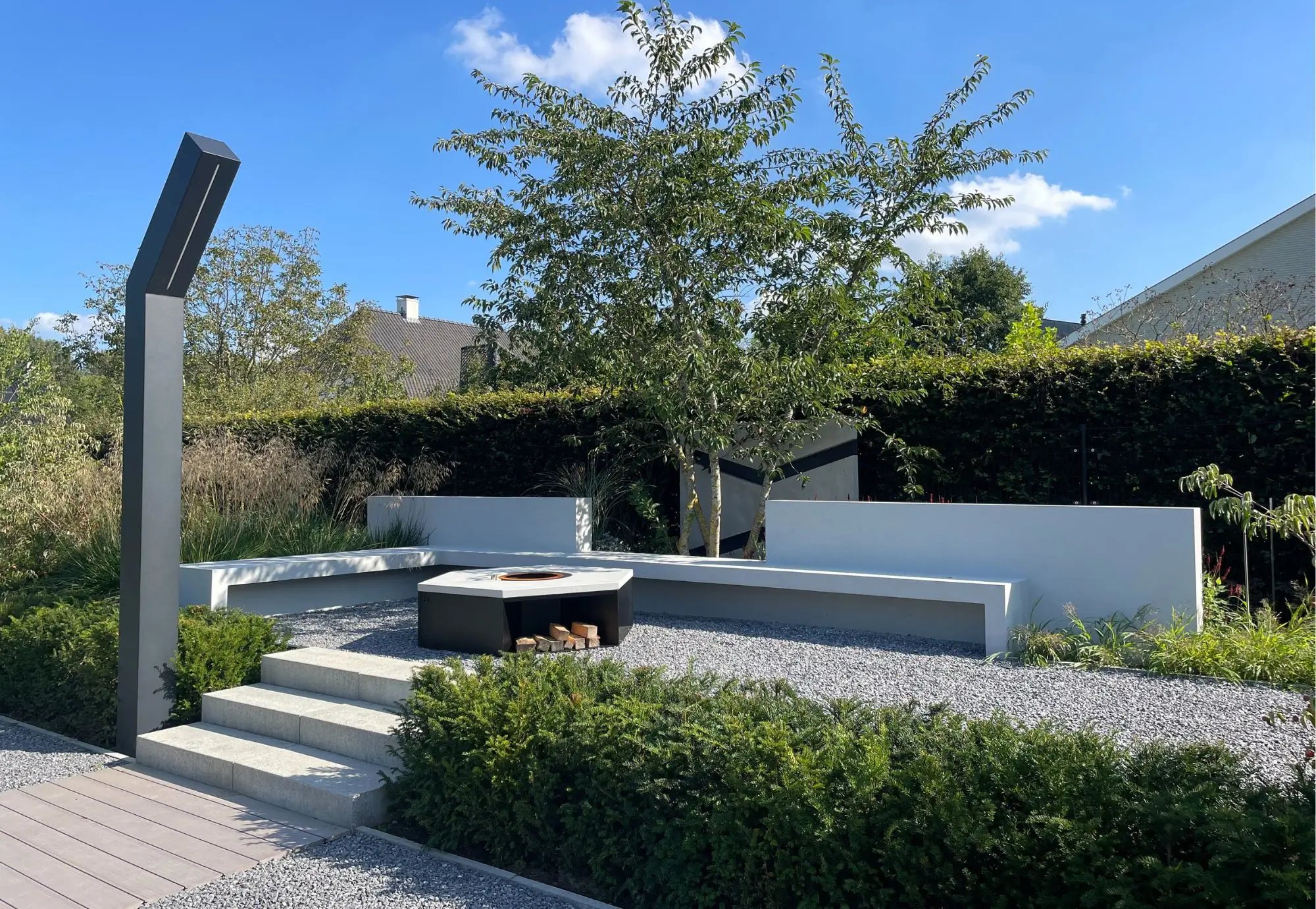 Loungeterras met een vuurelement in een designtuin. Met strakke wanden, weelderig groen, groene hagen, strakke materialen, solitaire heesters en unieke verlichting. Tuinontwerp en Tuinaanleg door Uw Tuin Hoveniers uit Malden.