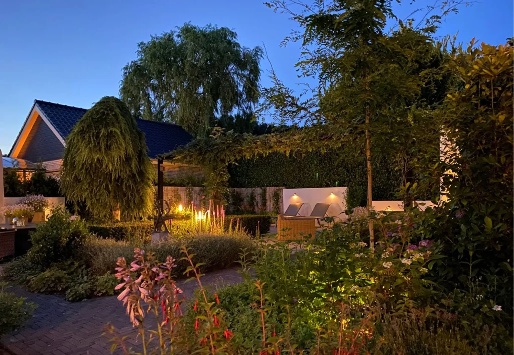 Achtertuin van moderne tuin met jacuzzi in Mook. In de avond sfeervol verlicht door het verlichtingsplan van Uw Tuin hoveniers uit Malden. Tuinontwerp en Tuinaanleg door Uw Tuin hoveniers. Veel groen