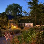 Achtertuin van moderne tuin met jacuzzi in Mook. In de avond sfeervol verlicht door het verlichtingsplan van Uw Tuin hoveniers uit Malden. Tuinontwerp en Tuinaanleg door Uw Tuin hoveniers. Veel groen
